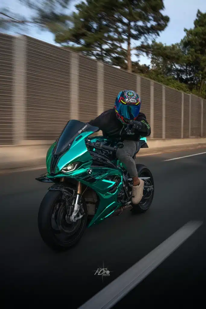 Motard en tenue noire sur une moto verte brillante en pleine accélération