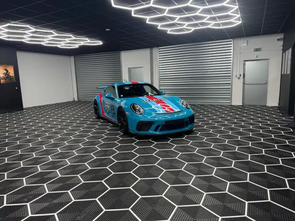 Porsche bleue Martini Racing dans un showroom au sol hexagonal